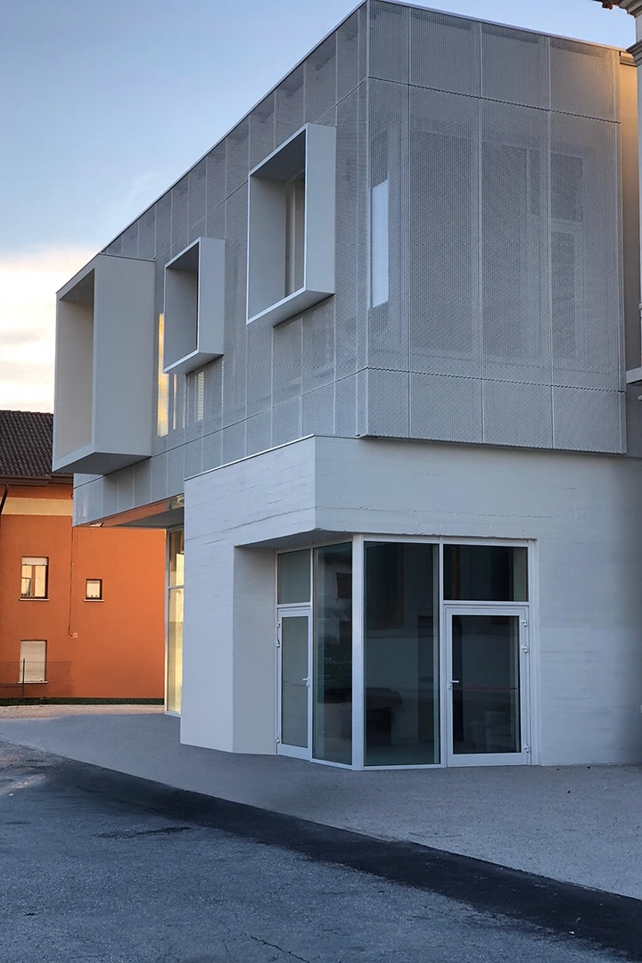 Edificio contemporaneo con rivestimento metallico microforato e volumi a sbalzo, ingresso vetrato al piano terra